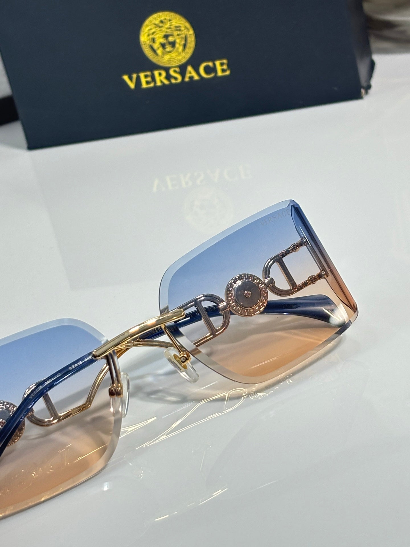 Versace sunglasses close-up of gold temple with logo medallion and blue-tinted lens