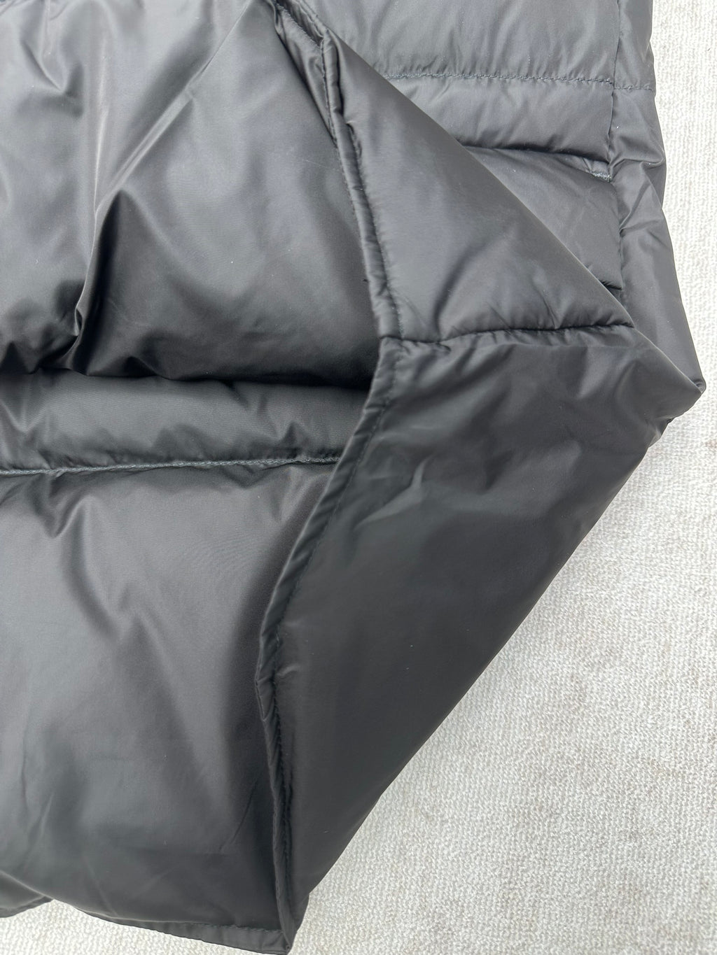 Black sleeveless puffer vest angled side view with curved quilting