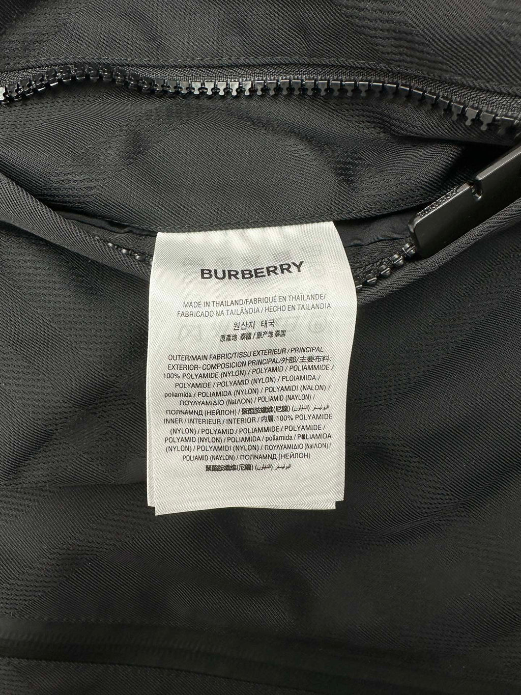 Fabric care label inside dark hooded puffer jacket near zipper