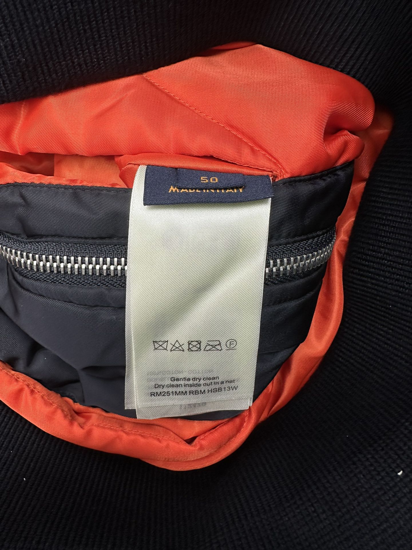 Navy bomber jacket with orange lining and interior size label near collar