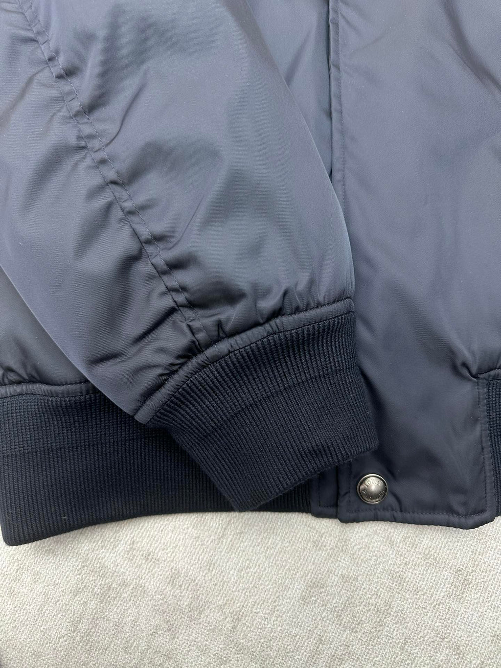 Navy bomber jacket sleeve with ribbed knit cuff and stitched seam detail
