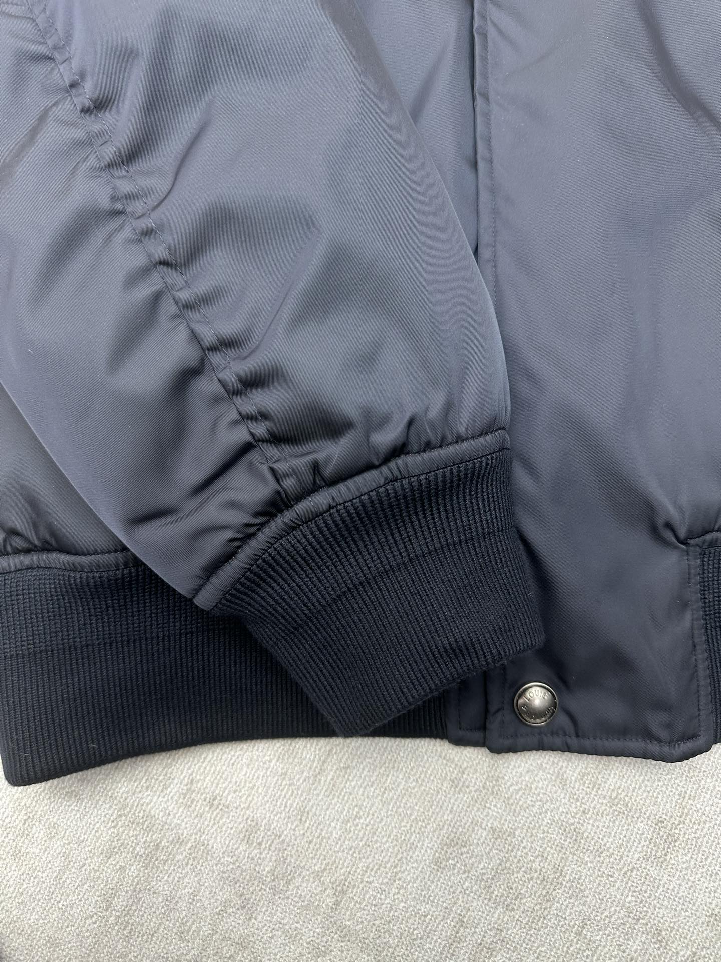 Navy bomber jacket sleeve with ribbed knit cuff and stitched seam detail
