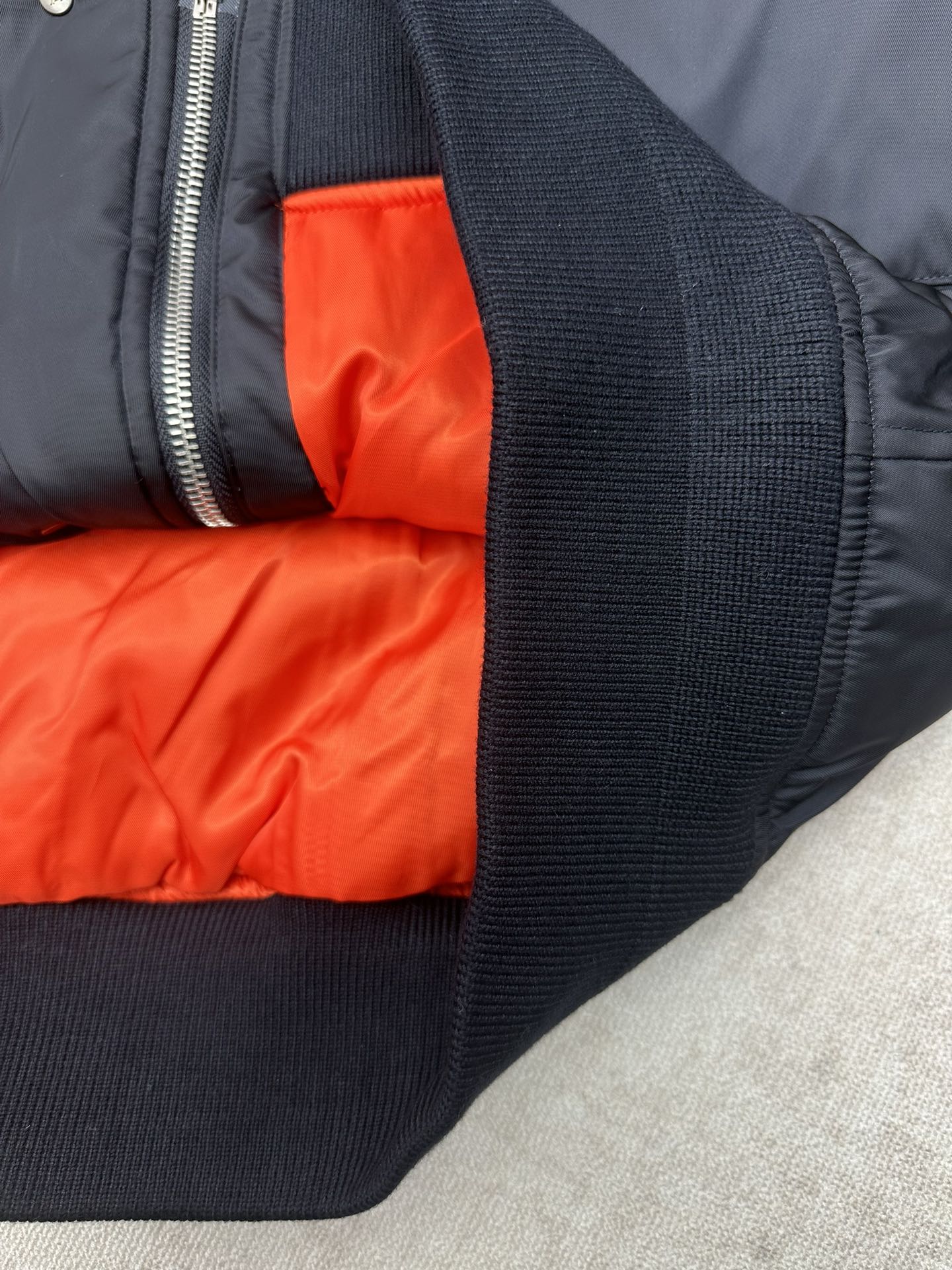 Navy bomber jacket sleeve cuff with bright orange interior lining near zipper