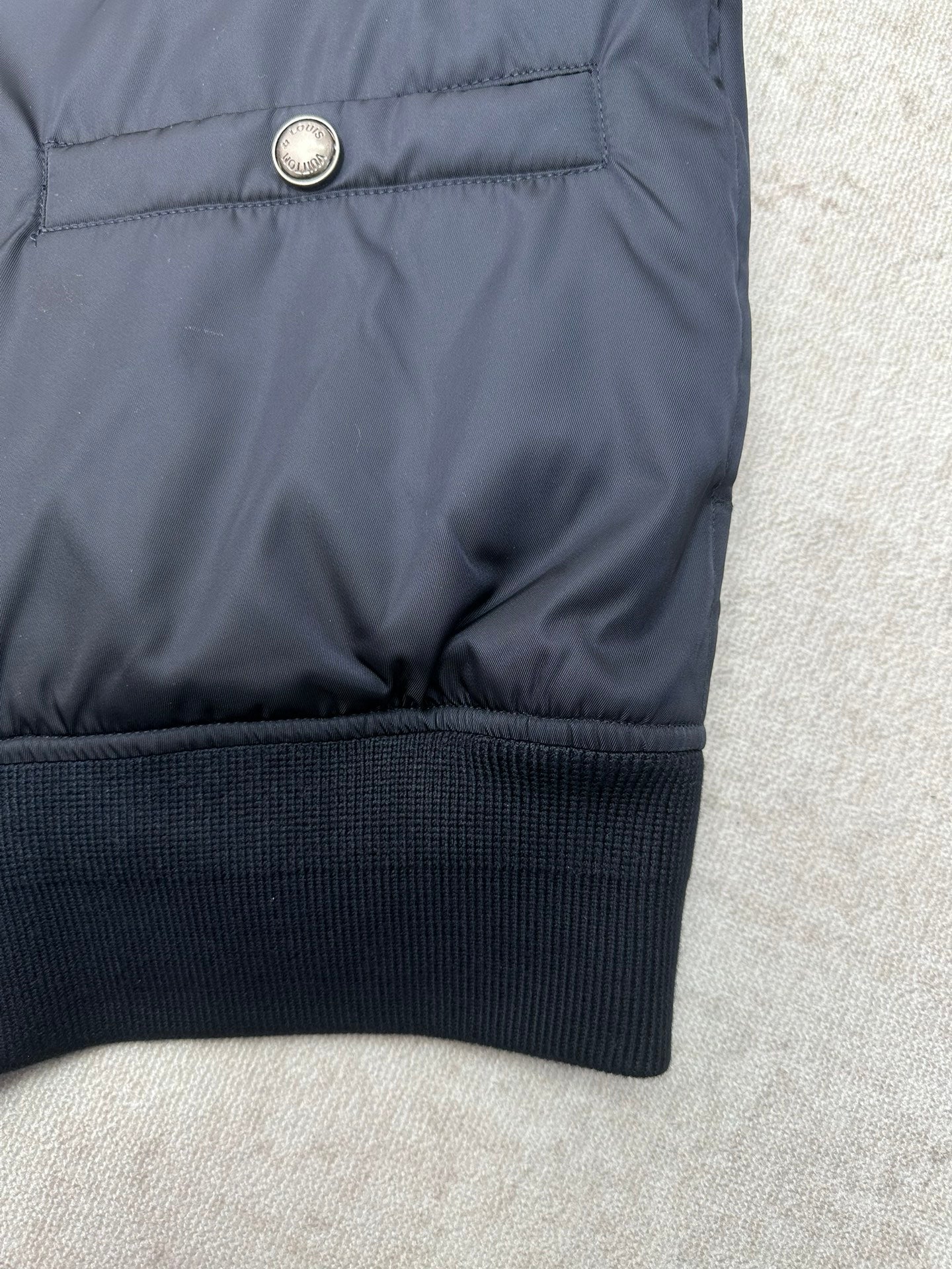 Navy bomber jacket hem with metal snap button at the upper back
