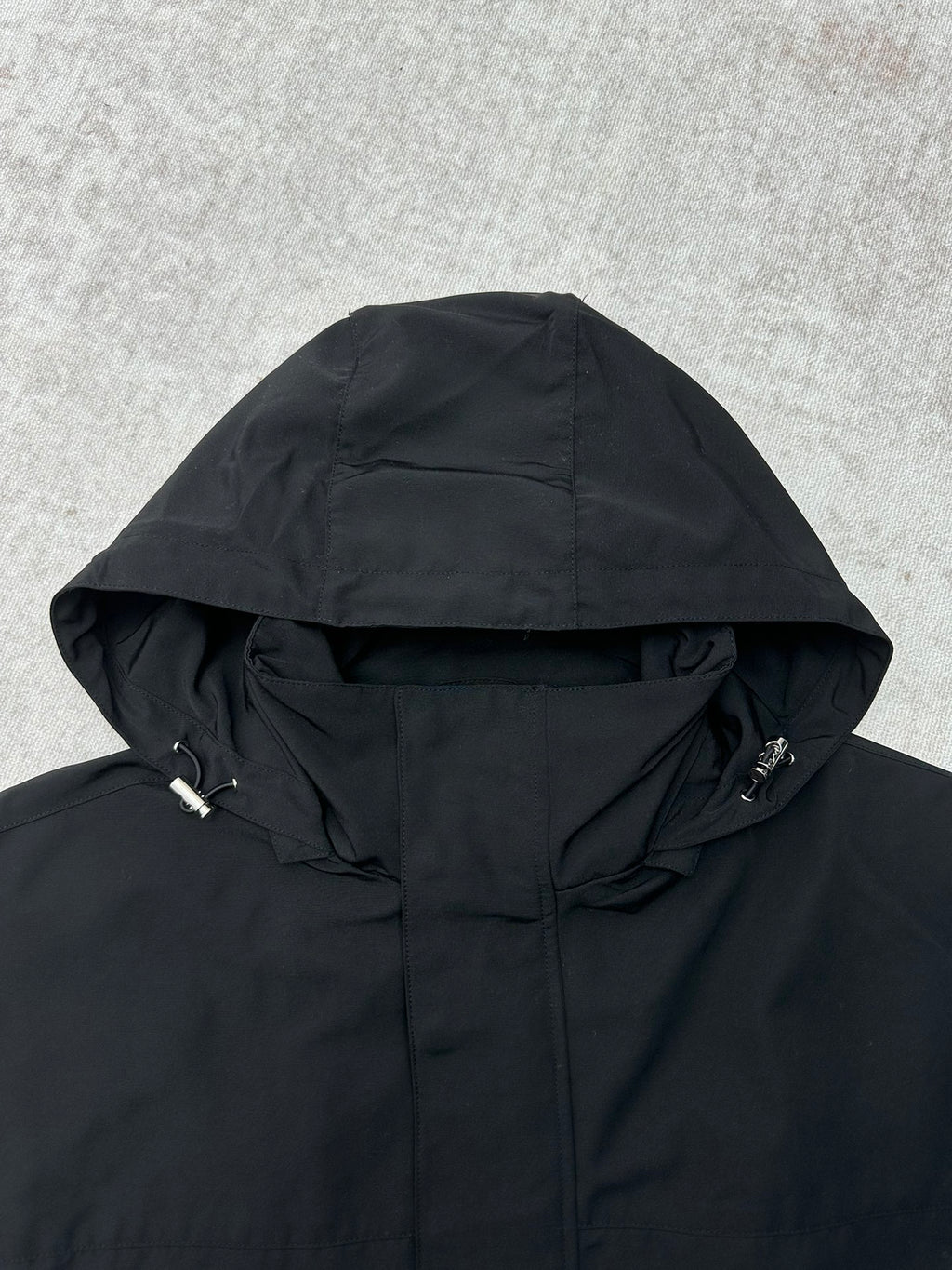 Dark hooded jacket with front zipper and adjustable draw cords