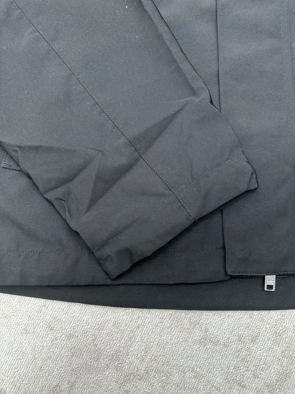 Dark jacket sleeve with seam lines and flap pocket detail