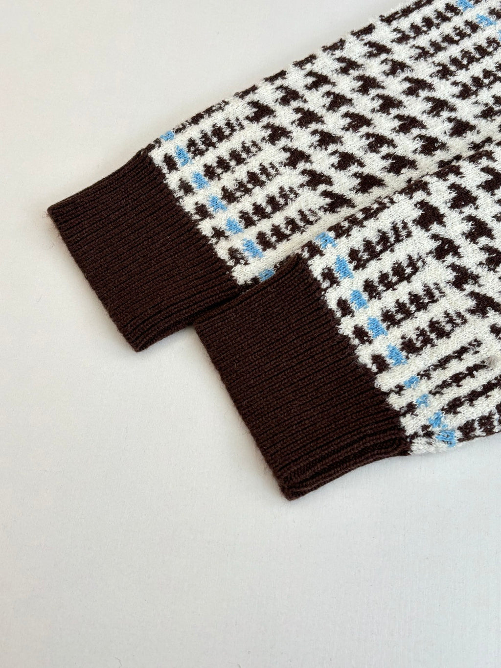 Bottom hem and ribbed cuff detail of check-pattern knit cardigan in brown