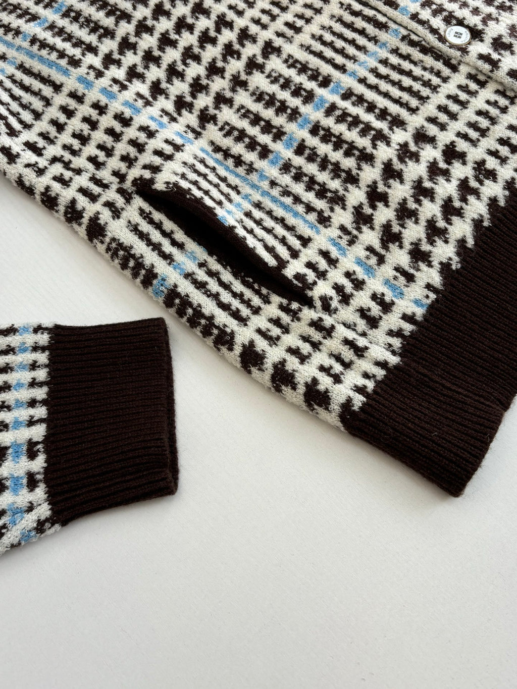Close-up of knit cardigan sleeve and ribbed cuff in check pattern with brown trim