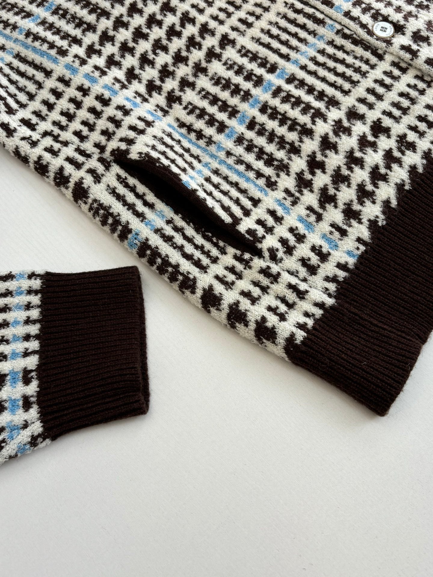 Close-up of knit cardigan sleeve and ribbed cuff in check pattern with brown trim