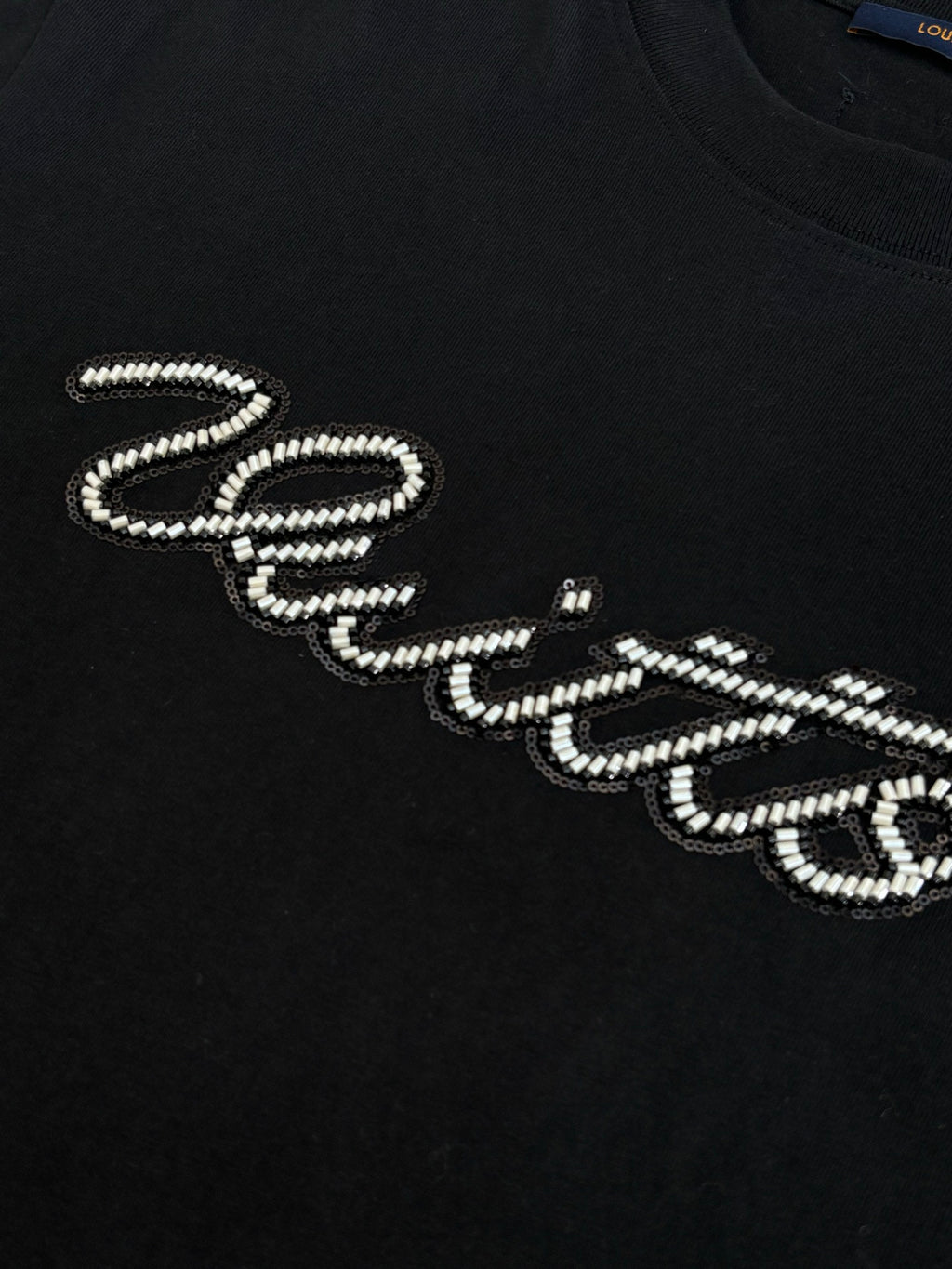 Louis Vuitton T-shirt detail: black top with rhinestone script lettering on the chest.