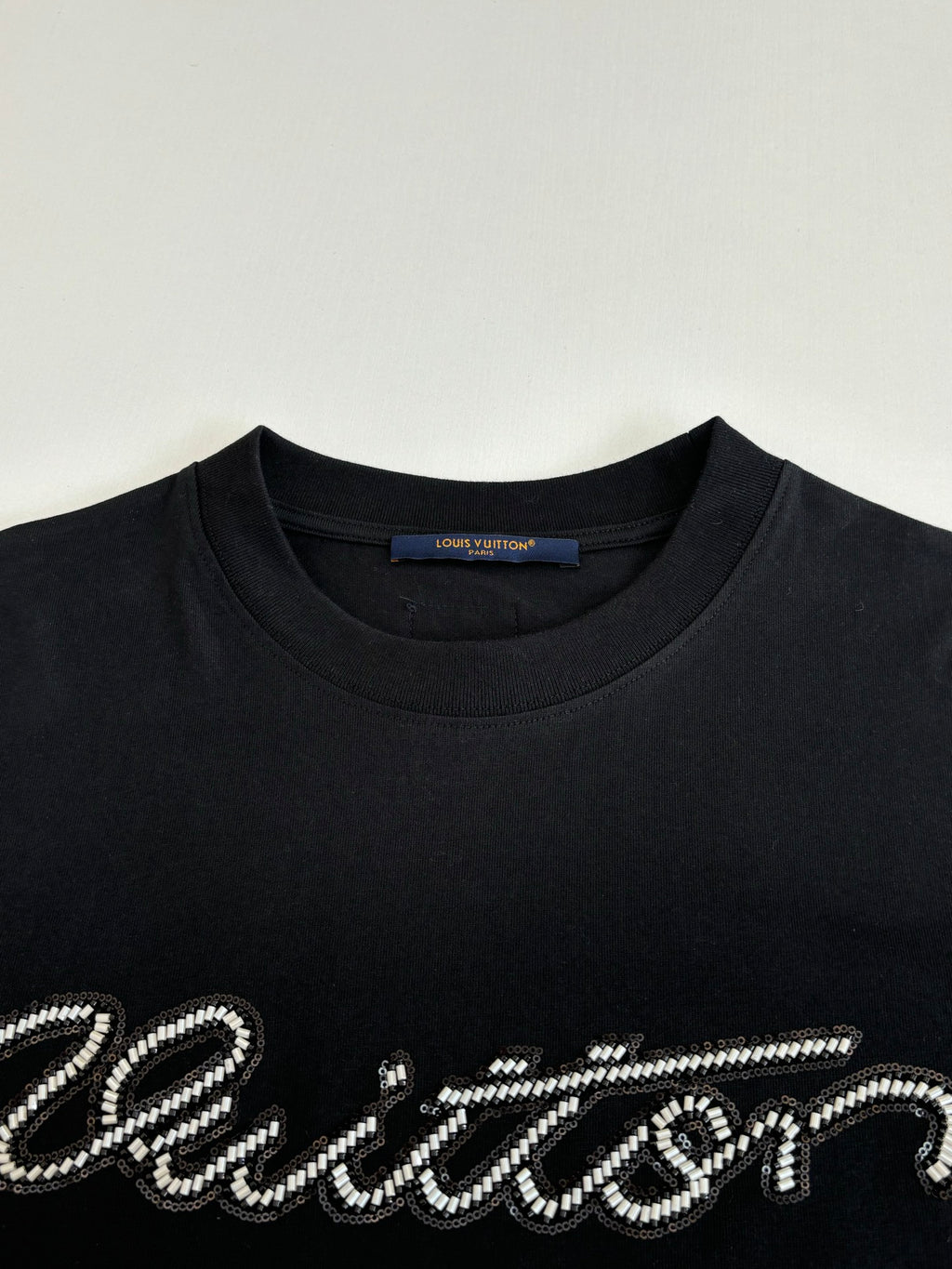 Louis Vuitton T-shirt close-up: black crew neck with embellished script logo.