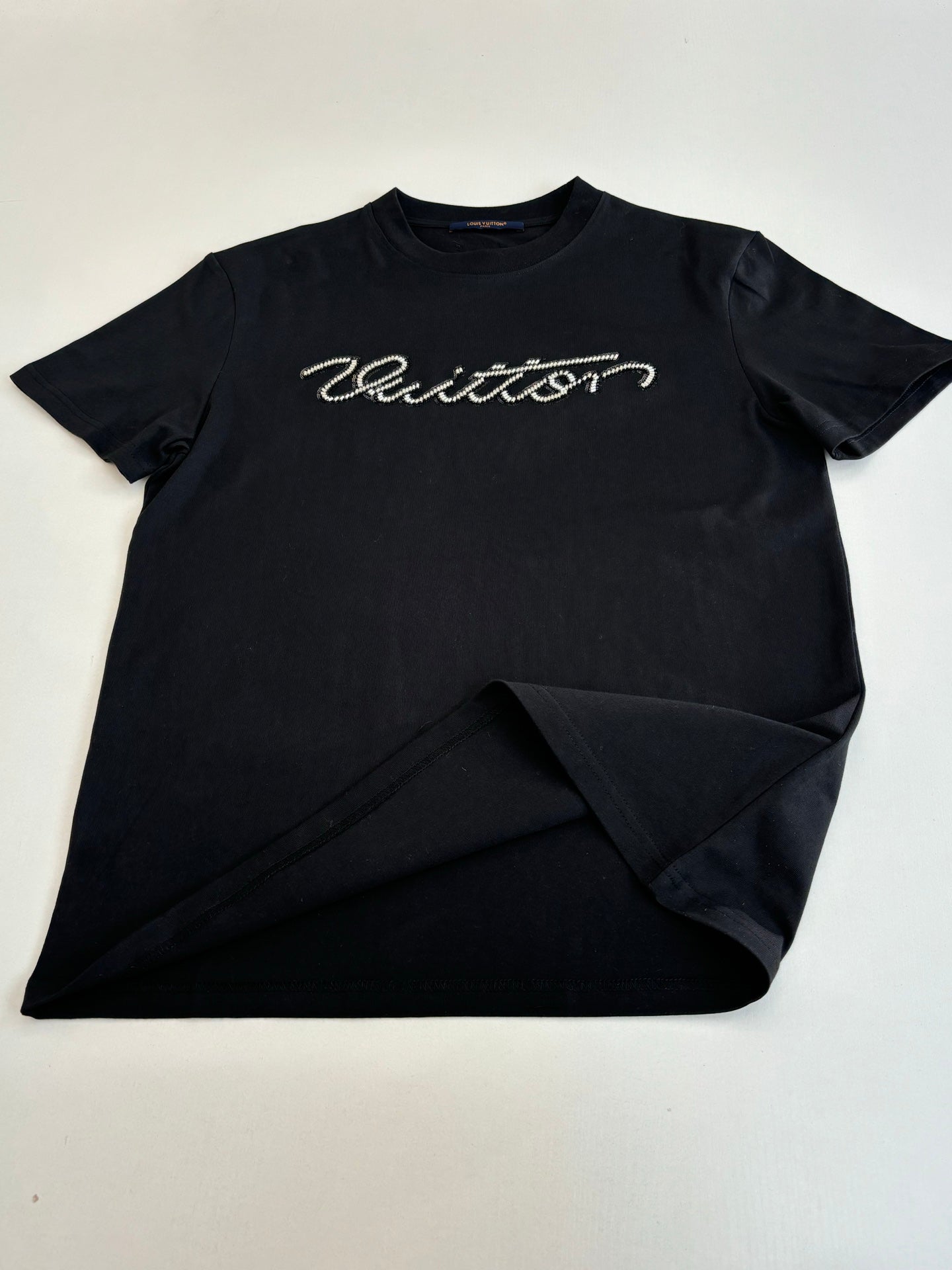 Louis Vuitton T-shirt, black with script logo on chest; laid flat with folded hem.