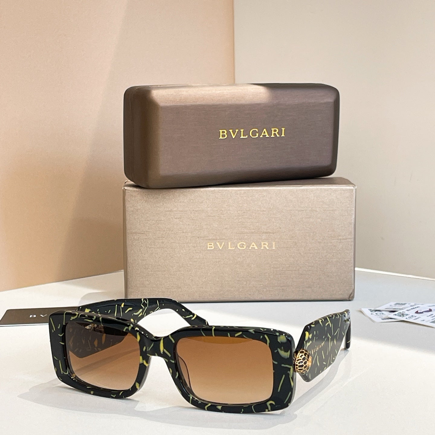 Dark patterned square sunglasses with amber lenses and gold logo emblem at temple