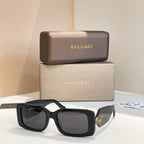 Black square sunglasses with dark lenses and gold logo charm on temple