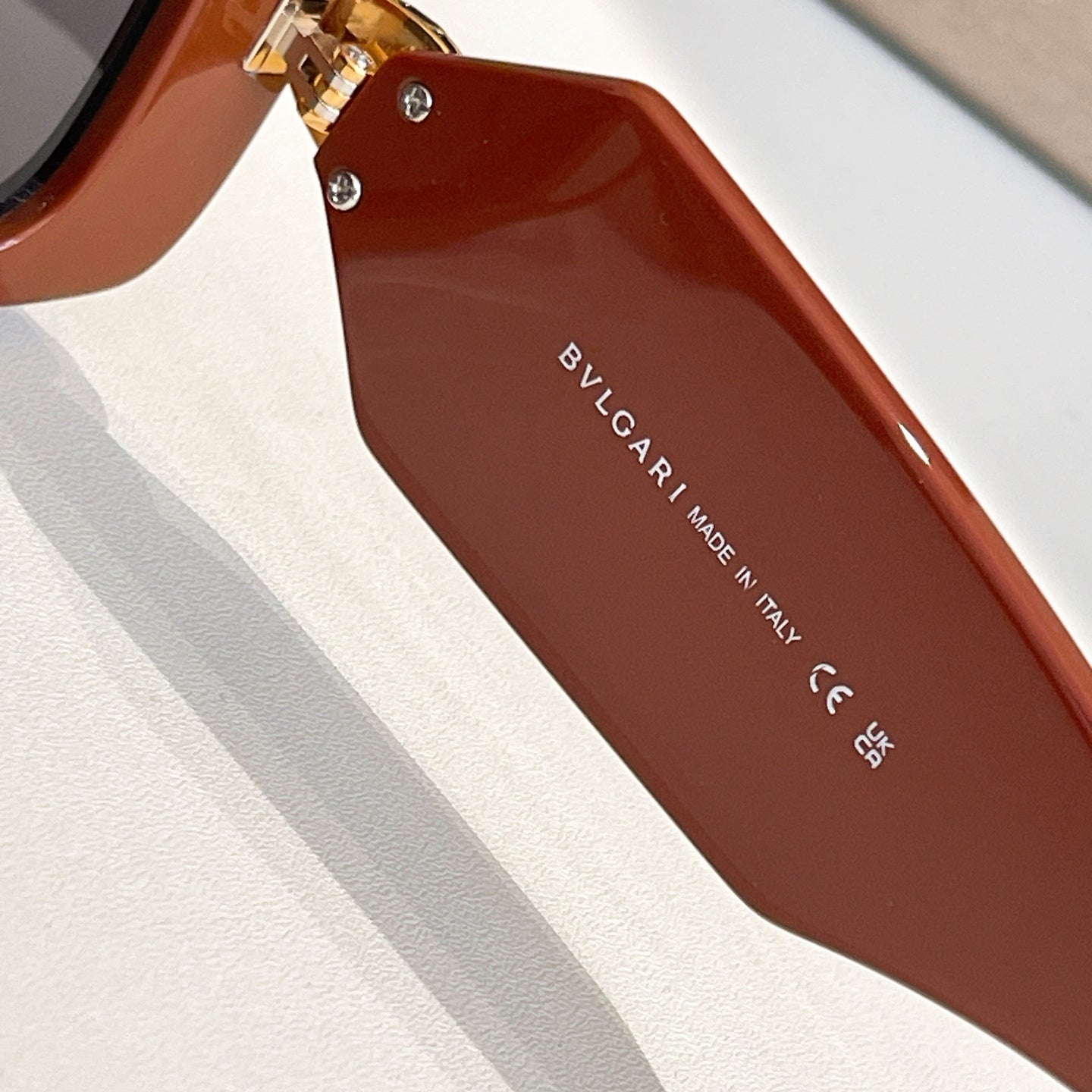 Brown square sunglasses closeup with gold emblem at temple and Bvlgari logo