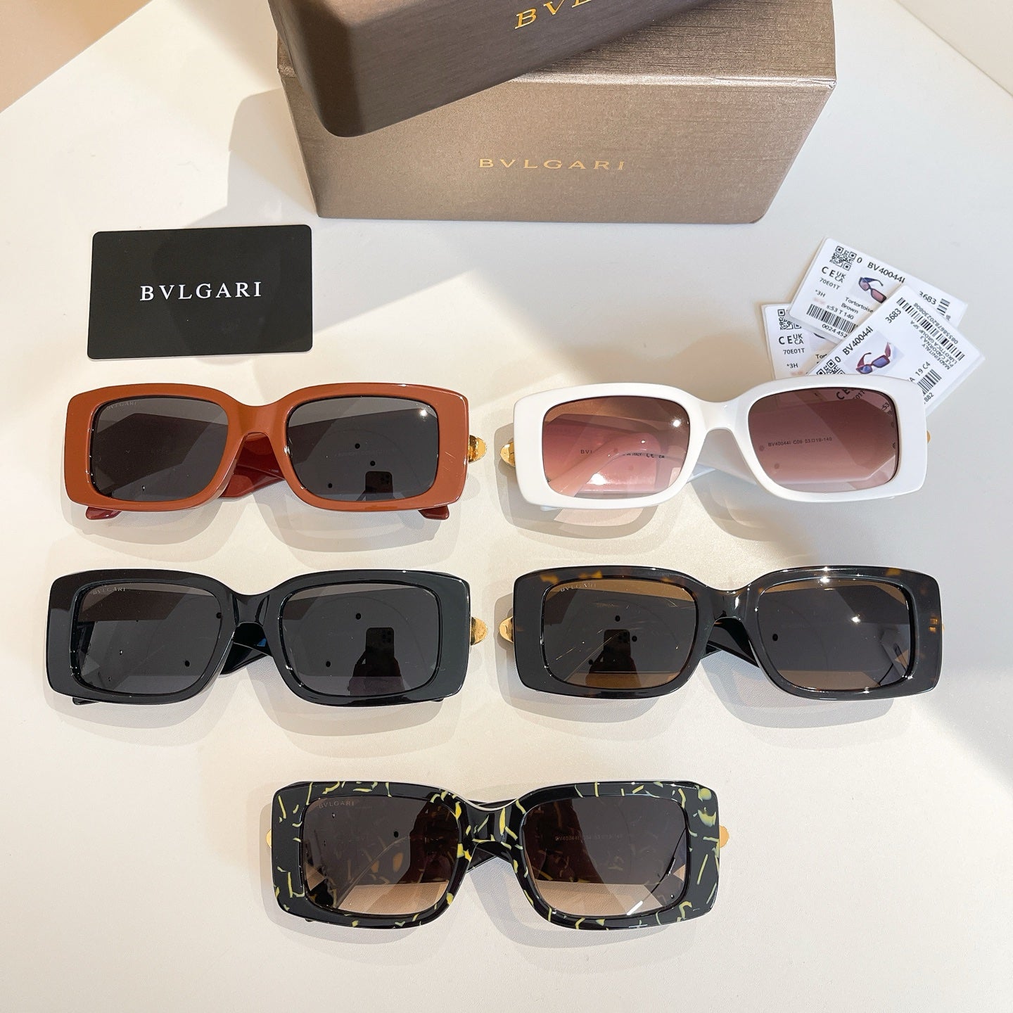 Assorted sunglasses: orange, white, black, and patterned frames with gold logo emblems