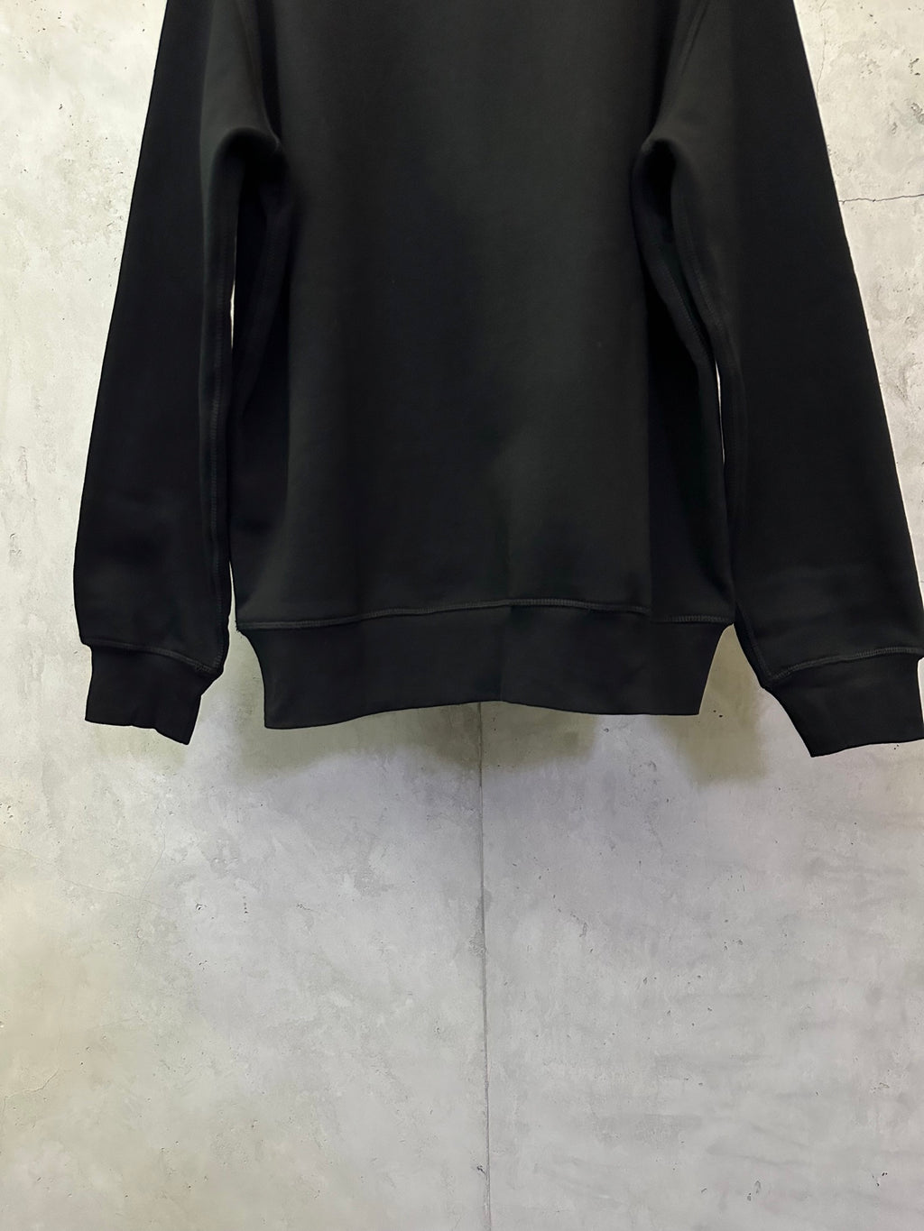 Black crewneck sweatshirt back view showing ribbed cuffs and hem