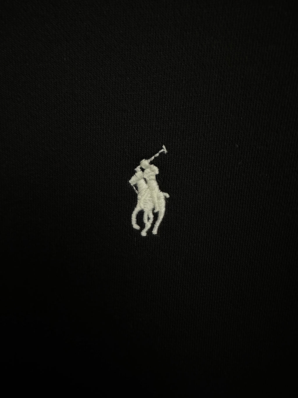 Small embroidered white Polo player logo on black sweatshirt fabric