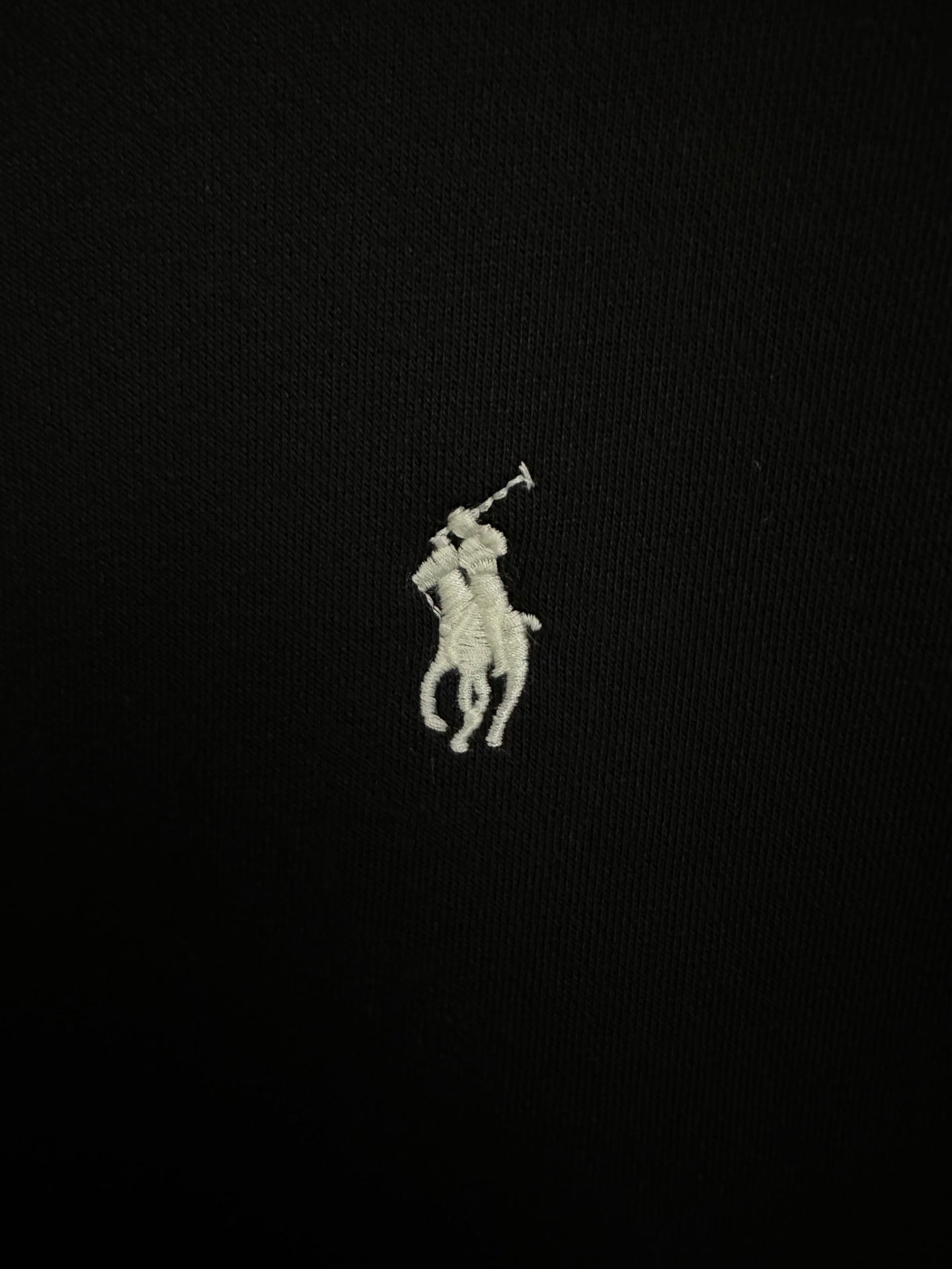 Small embroidered white Polo player logo on black sweatshirt fabric