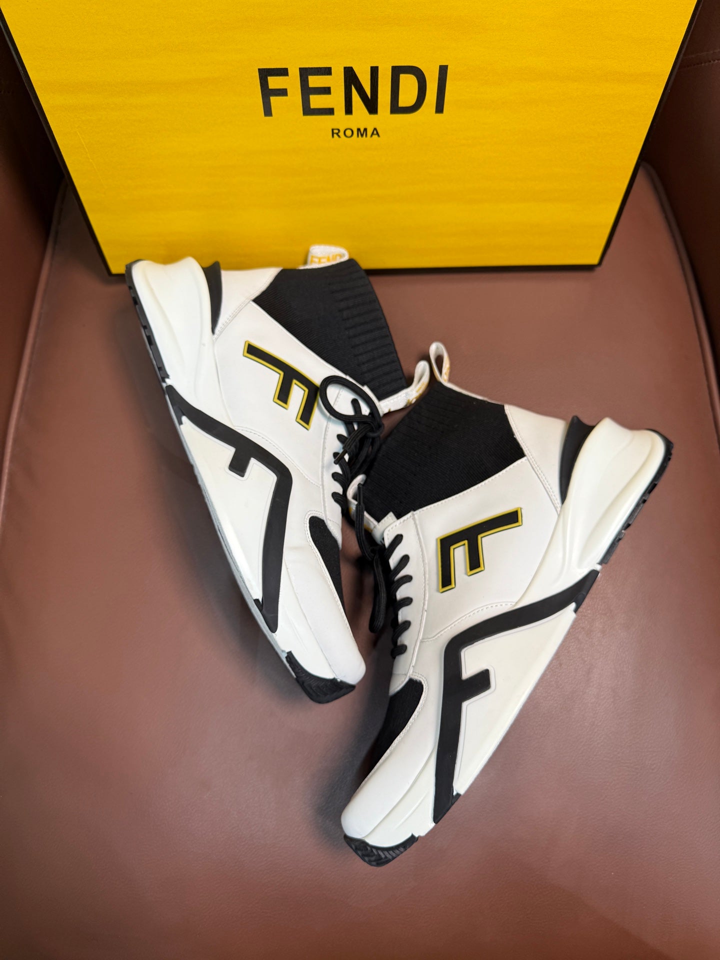 White and black high-top sneakers with black laces and gold-toned side lettering