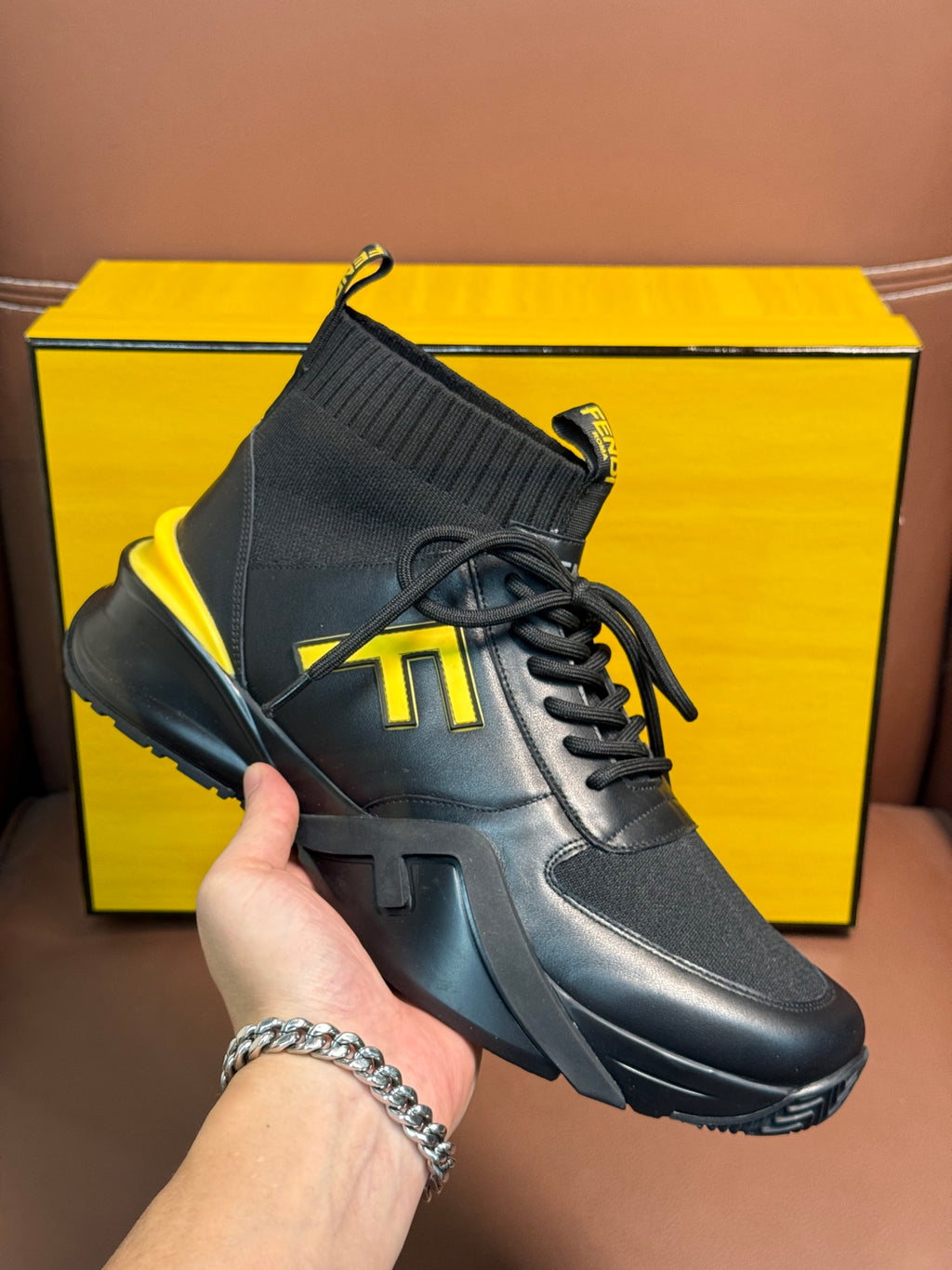 High-top sneaker on hand, dark gray leather-look upper with neon yellow logo accents