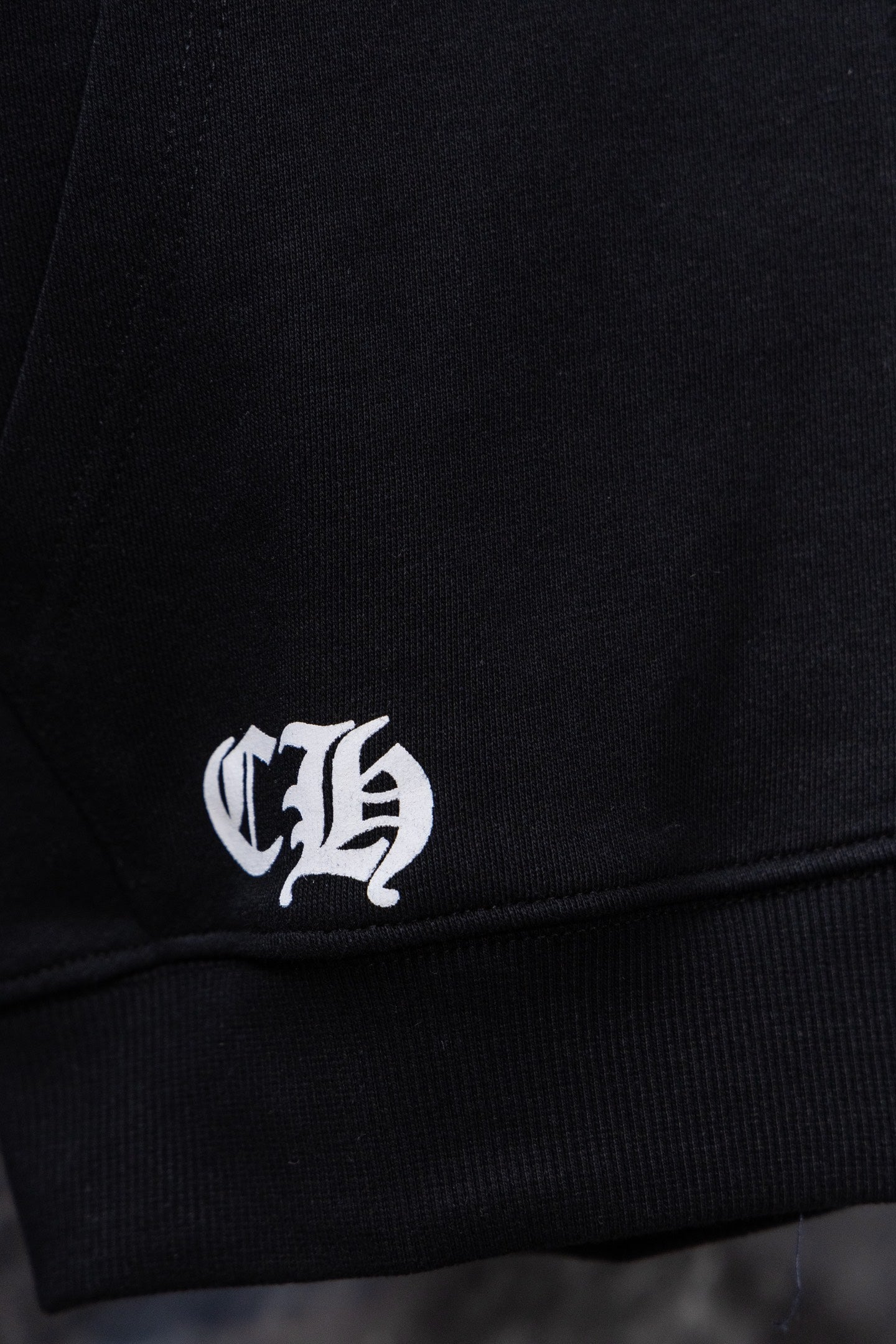 Black hoodie cuff with white logo embroidery near hem