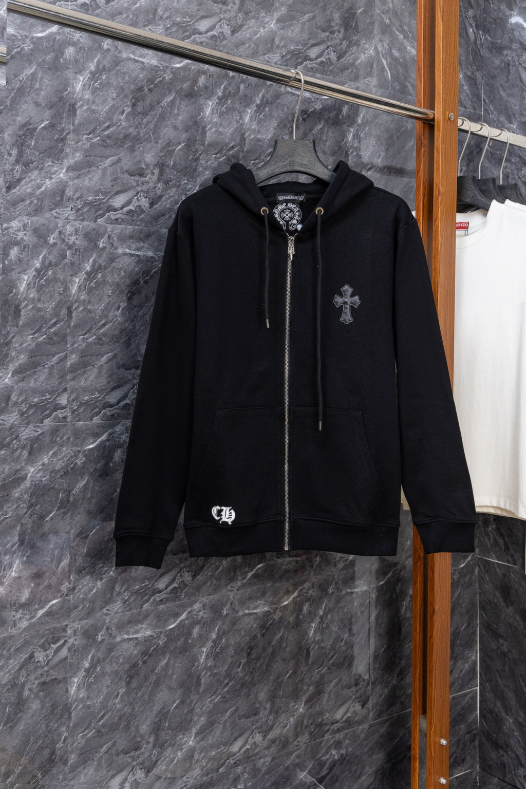 Black zip-up hoodie with front drawstring and small crest patch on chest