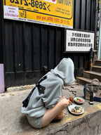 Gray hoodie with black bow-tie accents, hood up on model