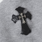 Embroidered black cross patch with metallic accents on light gray hoodie