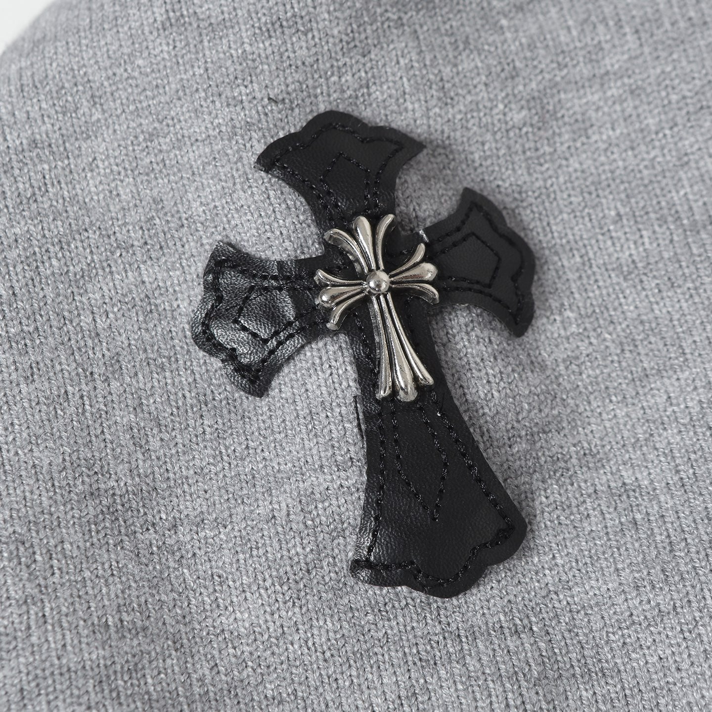 Embroidered black cross patch with metallic accents on light gray hoodie