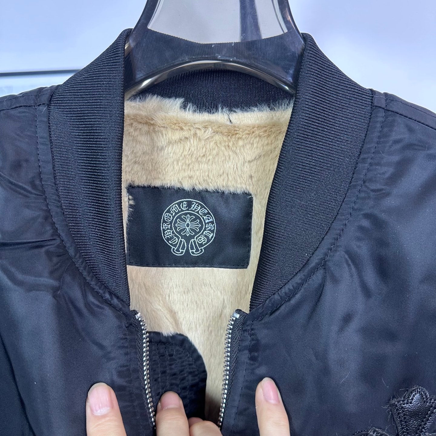 Long-sleeve bomber jacket interior with beige sherpa lining and blue logo label