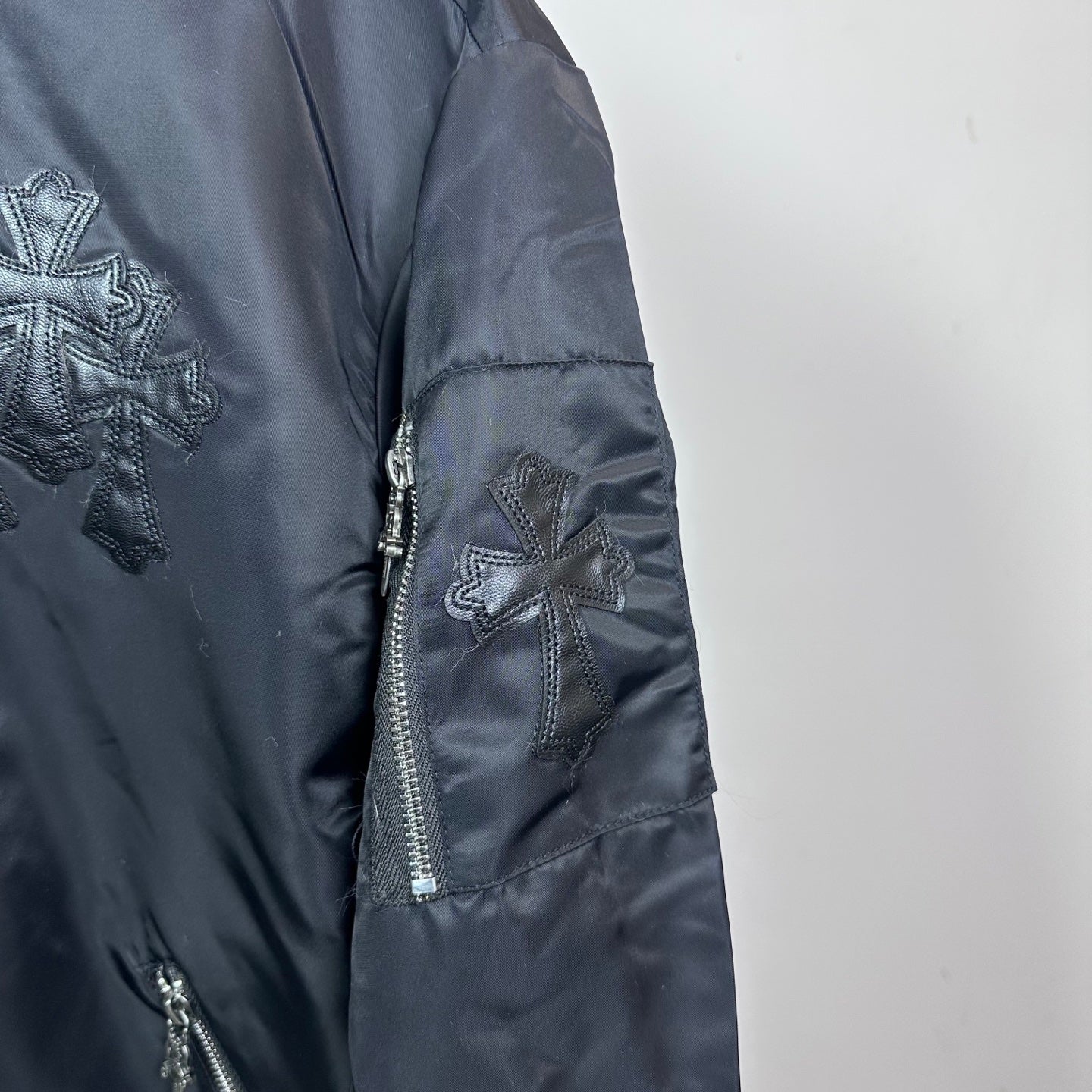 Dark blue bomber jacket sleeve with side zipper pocket and cross applique