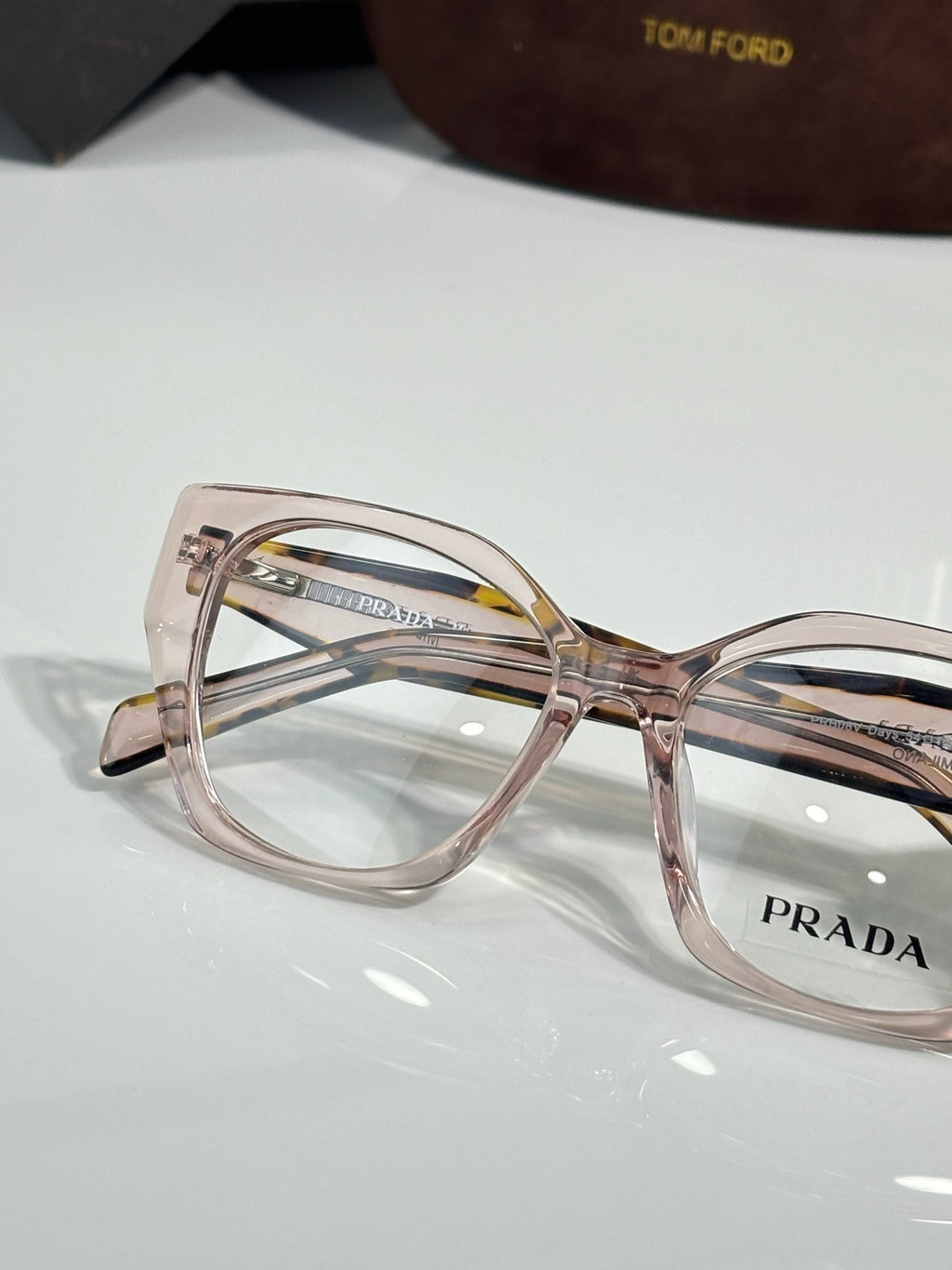 Prada eyeglass frame close-up with translucent pink front, clear lenses, logo on arm.