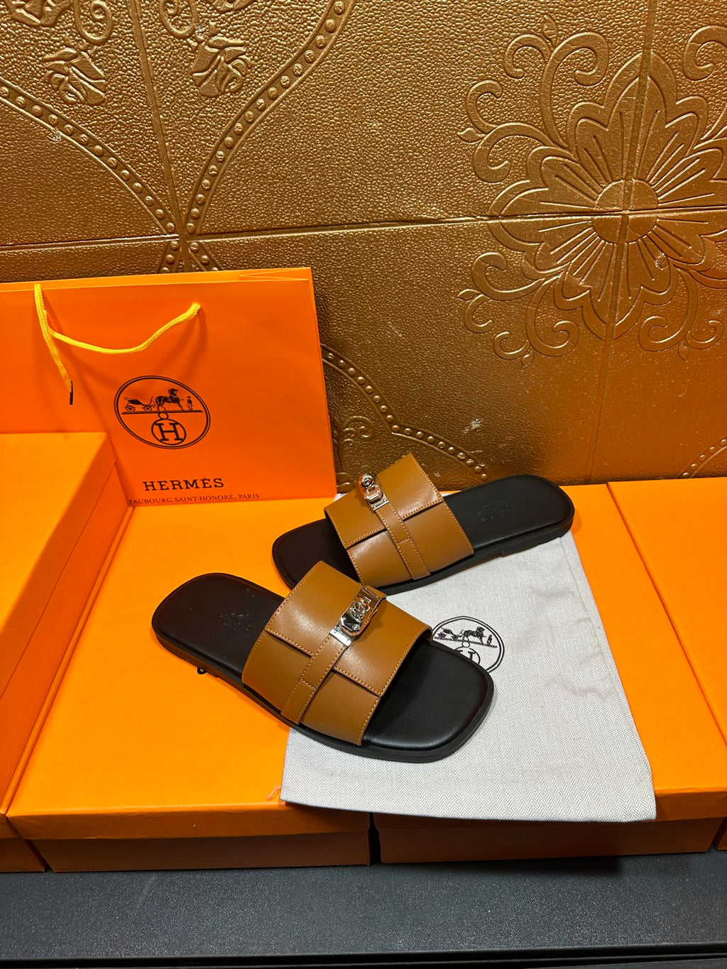 Tan leather sandals with two straps and silver metal buckle over black base
