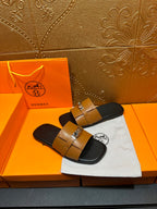 Tan leather sandals with two straps and silver metal buckle over black base