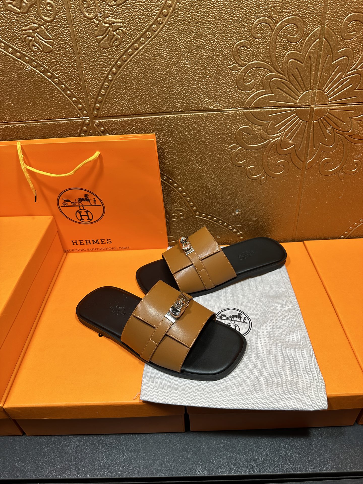 Tan leather sandals with two straps and silver metal buckle over black base