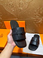 Hermes black leather slide sandal held in hand, wide strap with buckle