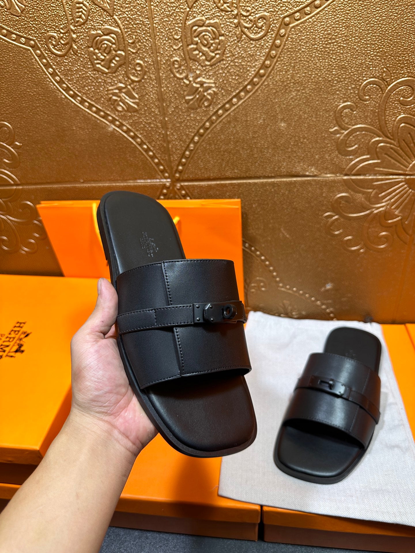 Hermes black leather slide sandal held in hand, wide strap with buckle