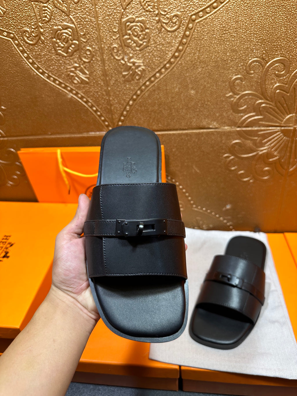 Hermes black leather slide sandal held up, wide strap and metal buckle detail