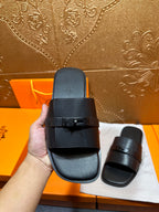 Hermes black leather slide sandal held up, wide strap and metal buckle detail