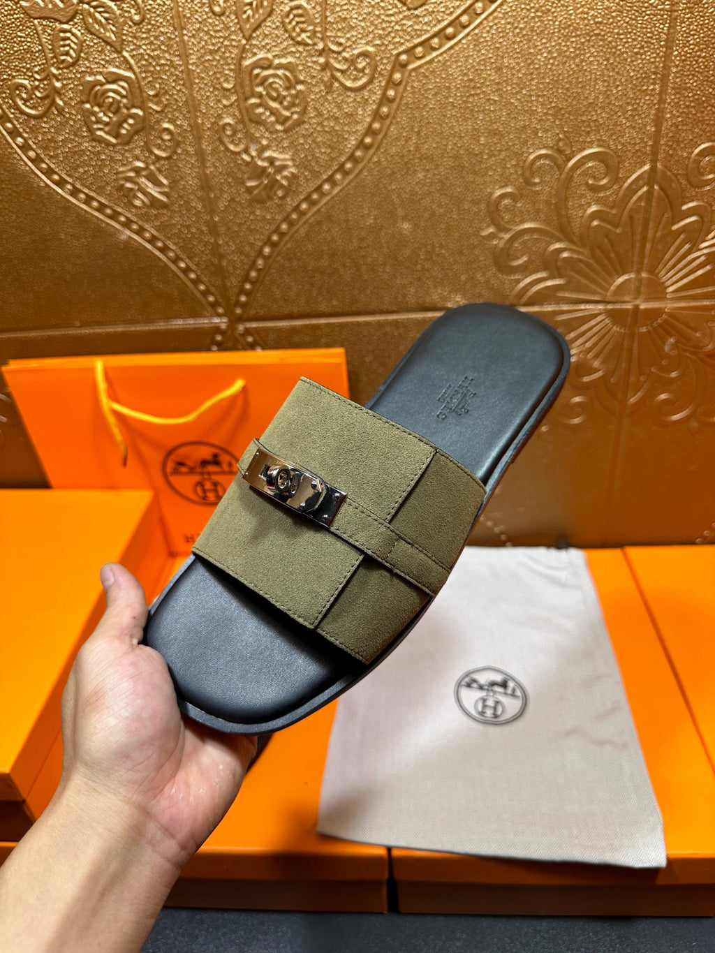 Hermes slide sandals in olive green held up, black footbed with silver buckle