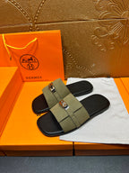 Pair of Hermes luxury slide sandals in olive green with silver buckle over black footbeds