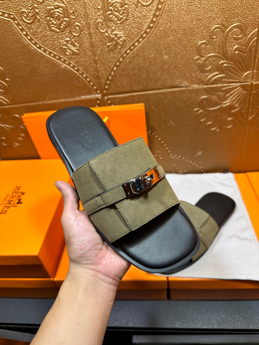Hand holding Hermes slide sandals in olive green with silver buckle and black footbed
