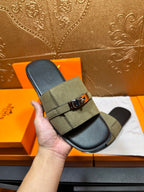 Hand holding Hermes slide sandals in olive green with silver buckle and black footbed