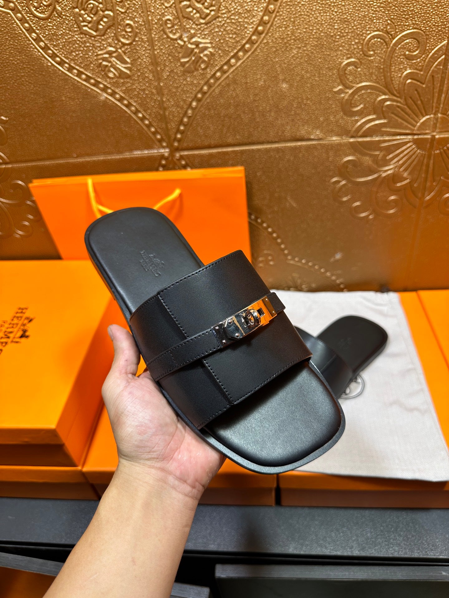Hermes luxury black sandal with wide strap and silver-tone buckle, held in hand