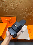 Navy leather slide sandals held in hand with gold-tone buckle