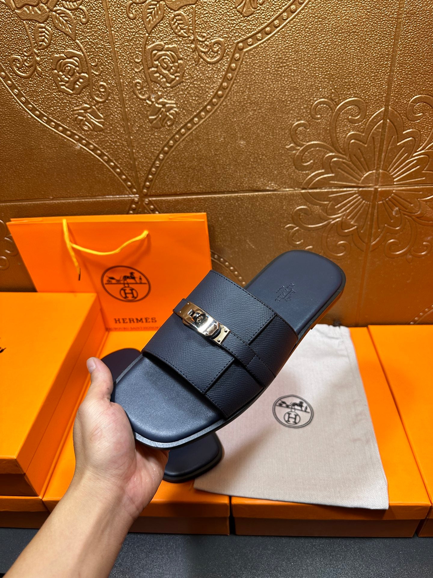 Navy leather slide sandals held in hand with gold-tone buckle