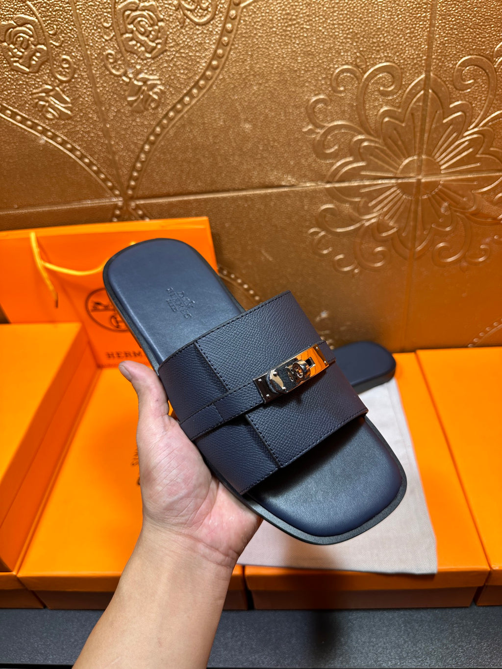 Navy leather slide sandal held in hand with gold-tone buckle strap