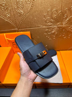 Navy leather slide sandal held in hand with gold-tone buckle strap