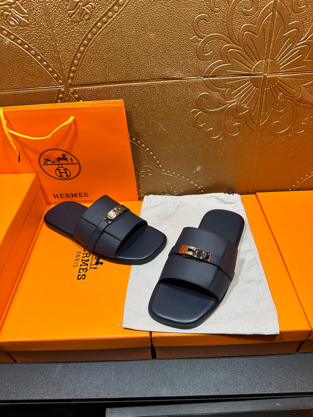 Navy leather slide sandals with gold-tone buckle, placed on white cloth